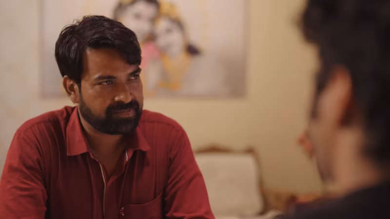 A bearded man in a red shirt, mid-argument across the table