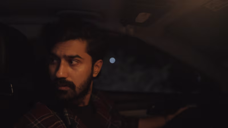 A man in a checked shirt looks over his shoulder from the driver seat at night