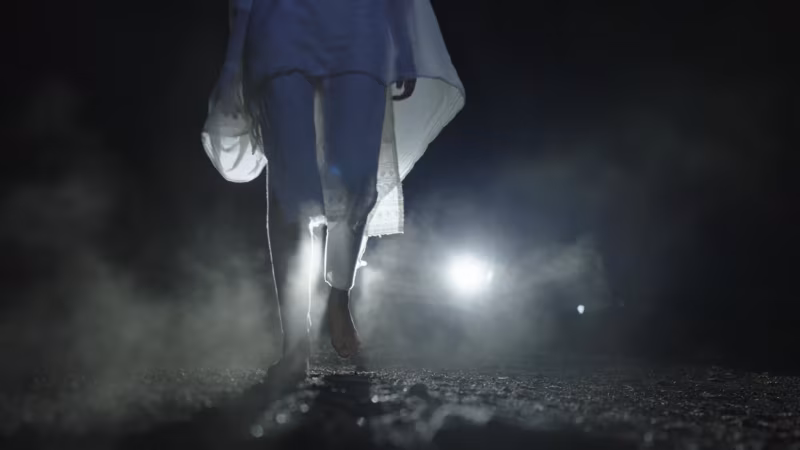 Bare feet walking away down the dirt road, a lamp burning in the haze behind