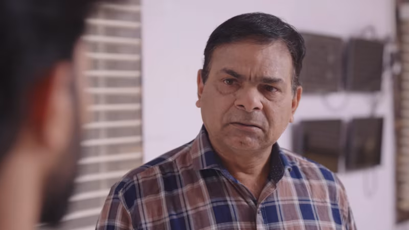 An older man in a checked shirt, mid-sentence
